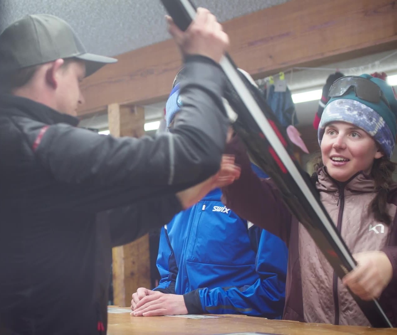 Three people are gathered around a table, examining and handling a pair of skis in Grand County Colorado.