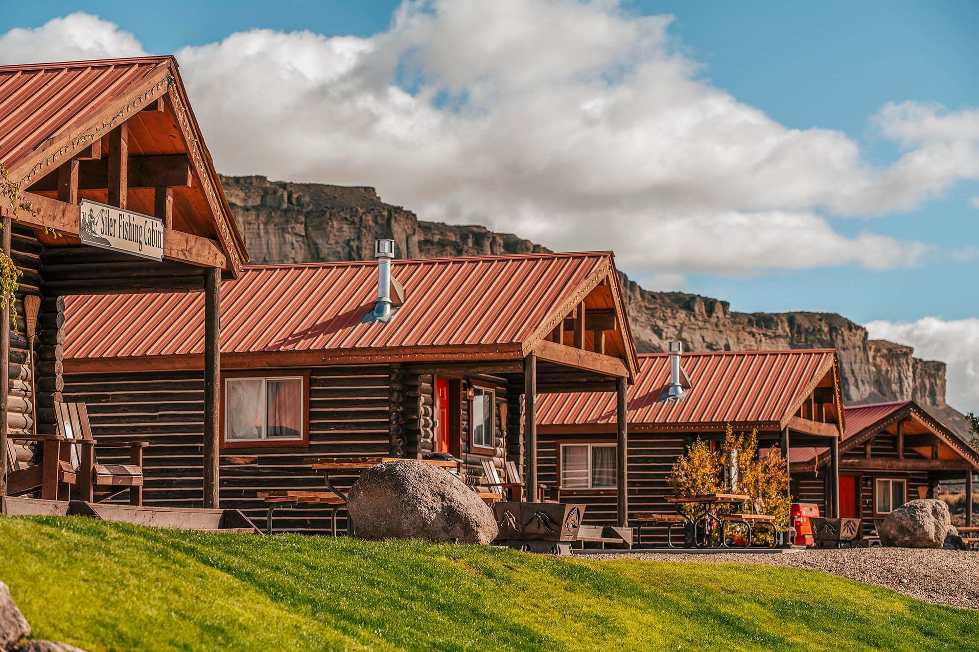 A row of rustic log cabins with red roofs nestled against a backdrop of towering cliffs in Grand County Colorado.