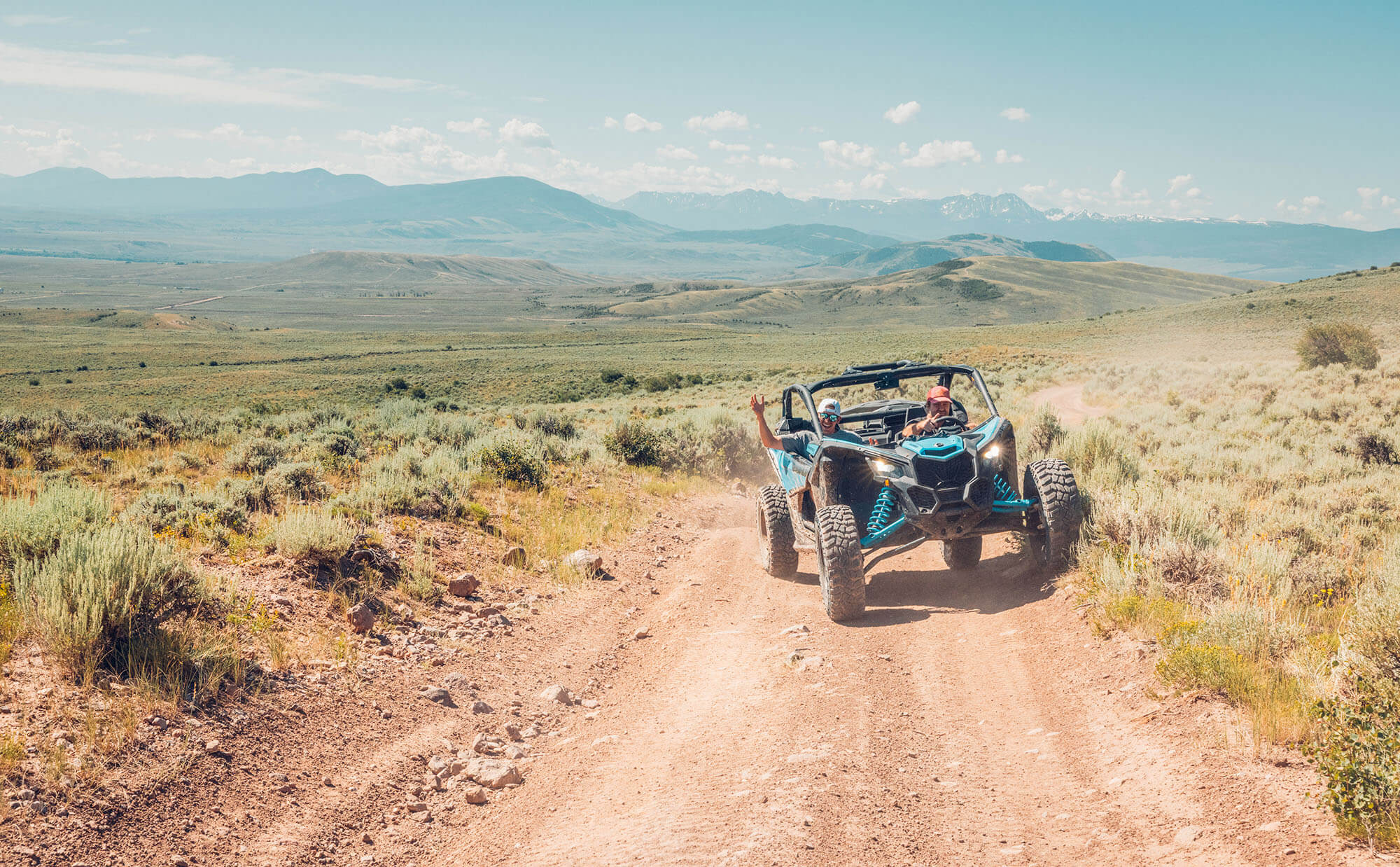 A blue off-road vehicle drives down a dirt road through a grassy field with mountains in the distance in Grand County Colorado.