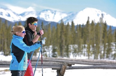 A couple enjoys cross-country skiing on a snowy trail with mountain views in Grand County Colorado.