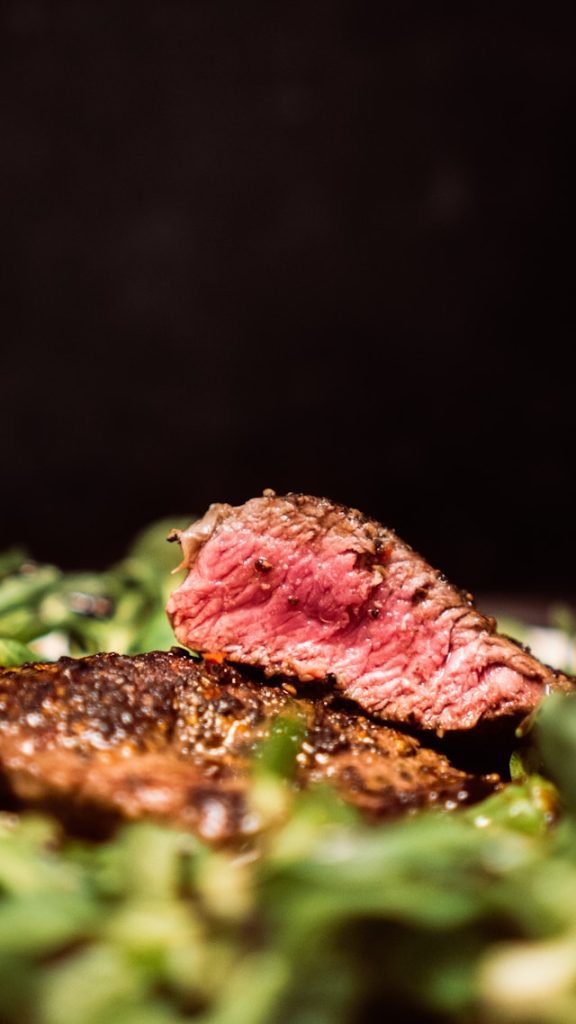 A close-up of a sliced medium-rare steak on a bed of greens with a dark background.