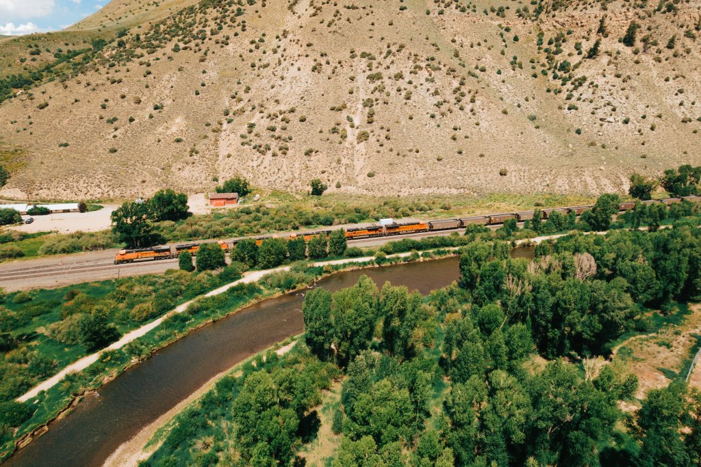 Aerial view of a train traveling along a river with mountains and forests in the background in Grand County Colorado.