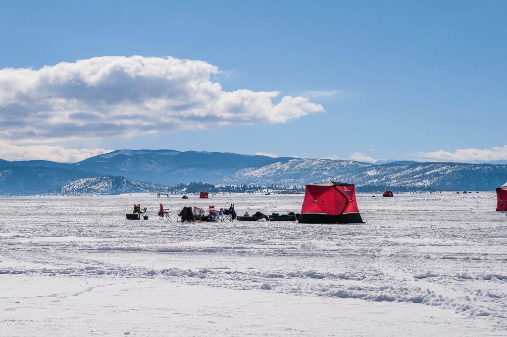 A vast expanse of snow-covered ice stretches out to the horizon, dotted with colorful ice fishing tents and equipment in Grand County Colorado.