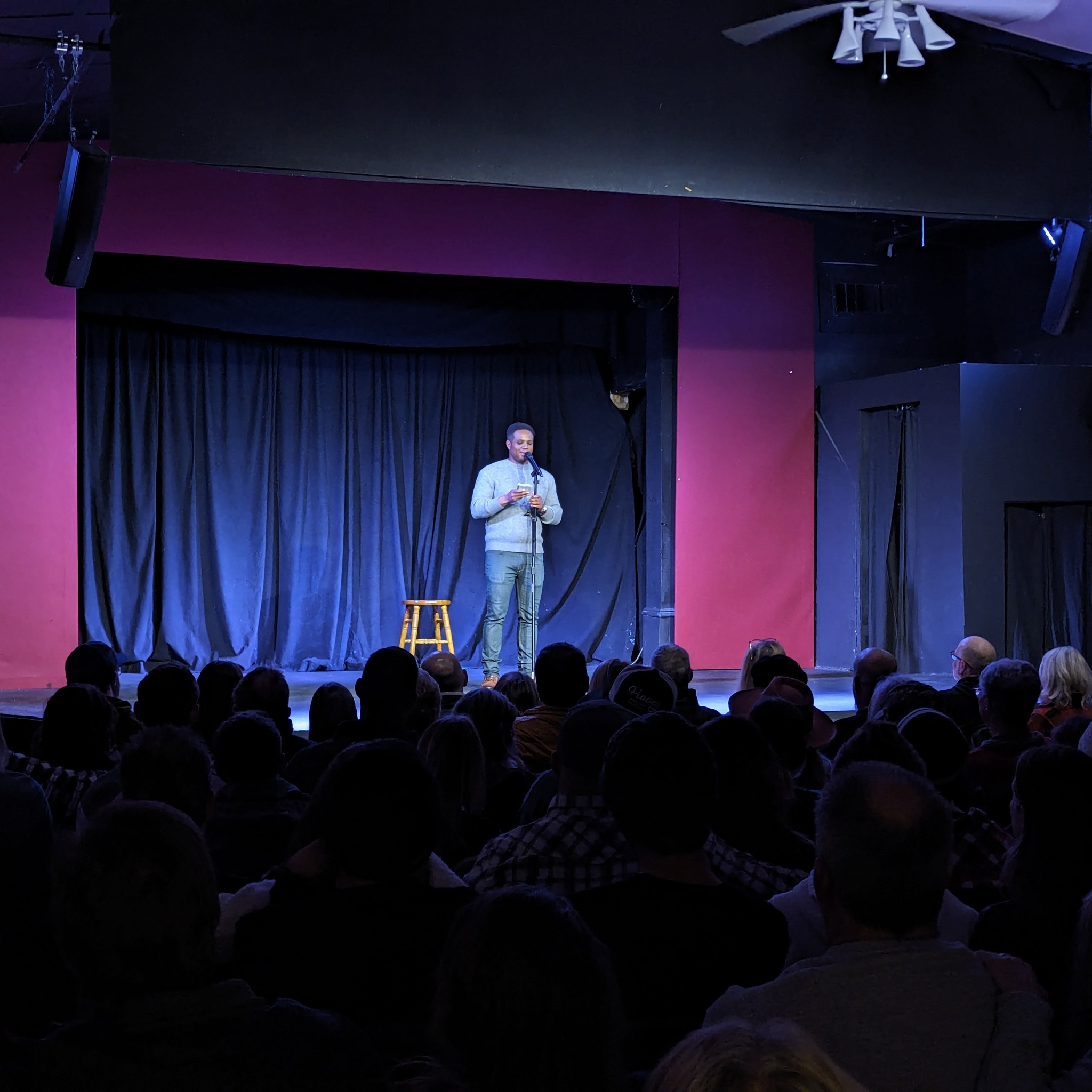 A man performs stand-up comedy on a stage before a seated audience in Grand County Colorado.
