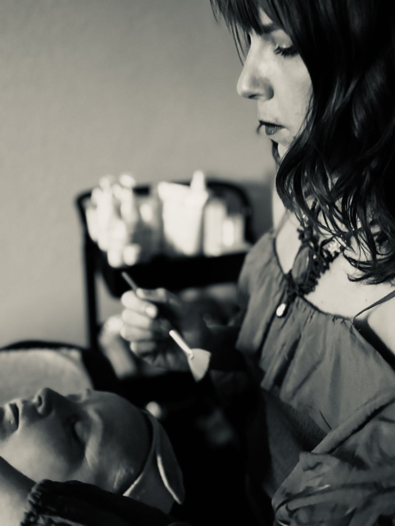 A woman with long hair is carefully applying makeup to a mannequin's face, focusing intently on her work in Grand County Colorado.