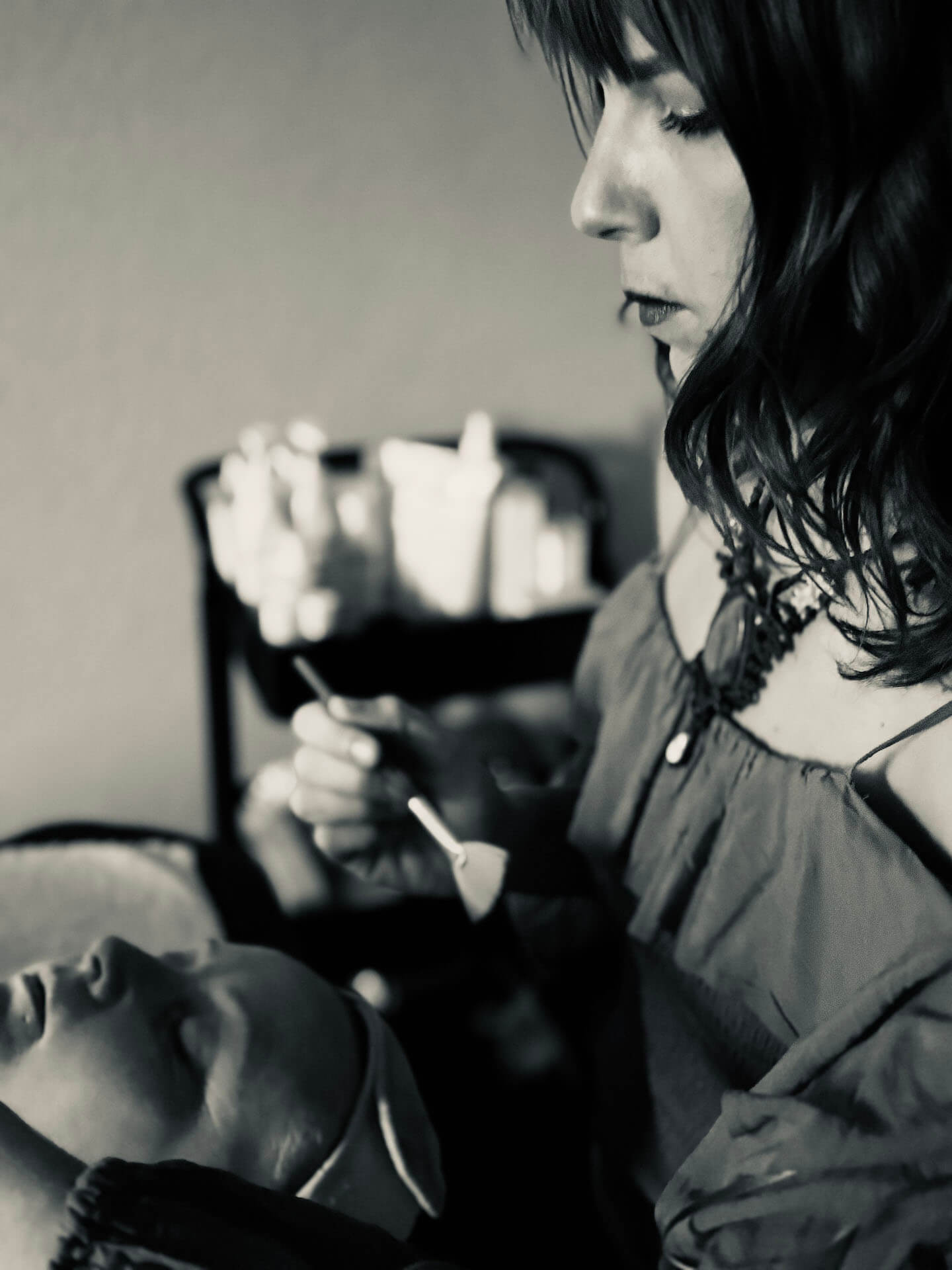 A woman with long hair is carefully applying makeup to a mannequin's face, focusing intently on her work in Grand County Colorado.