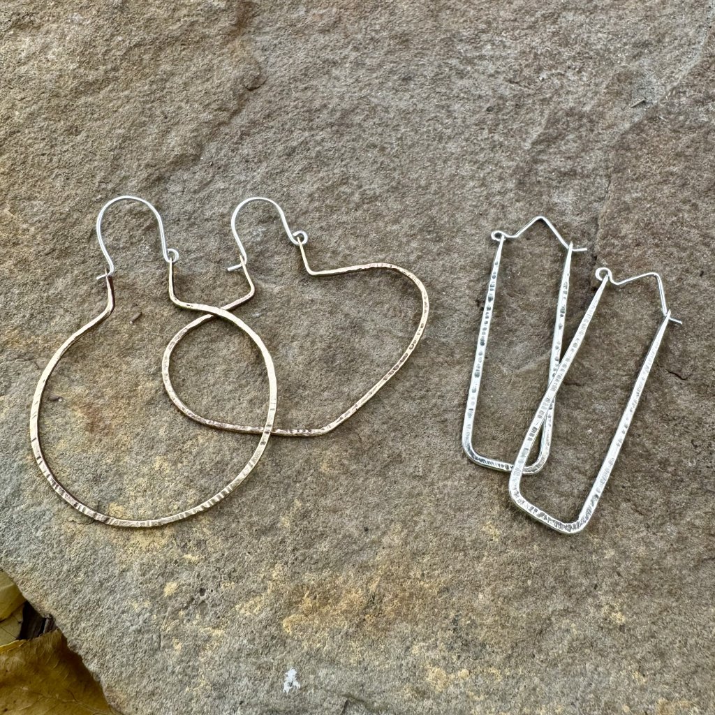 Three pairs of handmade earrings with unique shapes and textures are displayed on a textured stone surface in Grand County Colorado.