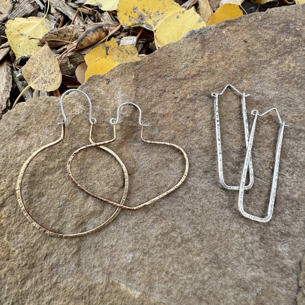 Three pairs of handmade earrings with unique shapes and textures rest on a textured stone surface surrounded by autumn leaves in Grand County Colorado.