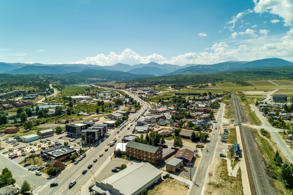 A picturesque town nestled in a valley with a backdrop of majestic mountains, surrounded by lush greenery and a network of roads and railways in Grand County Colorado.