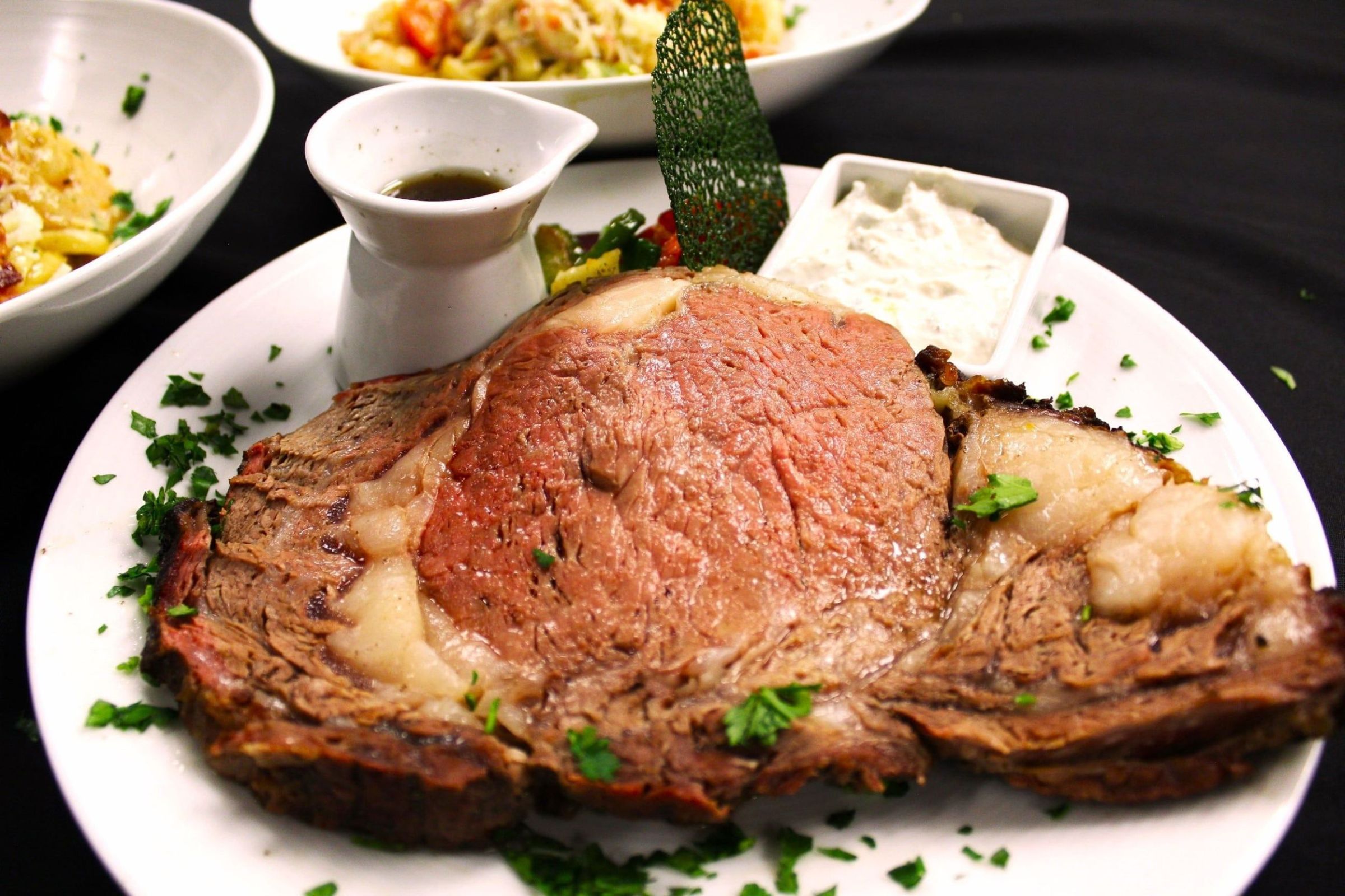 A succulent prime rib roast with a pink center, garnished with fresh herbs and served with au jus and horseradish cream on a white plate in Grand County Colorado.
