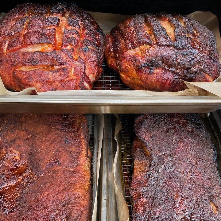 Four trays of smoked meats, including two large hams and two slabs of ribs, with a rich, dark bark in Grand County Colorado.