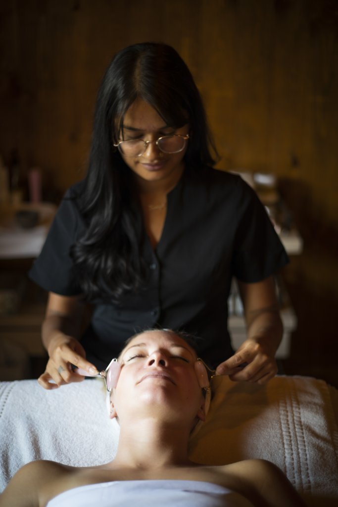 A woman with long dark hair and glasses is performing a facial massage on a client lying on a spa table in Grand County Colorado.