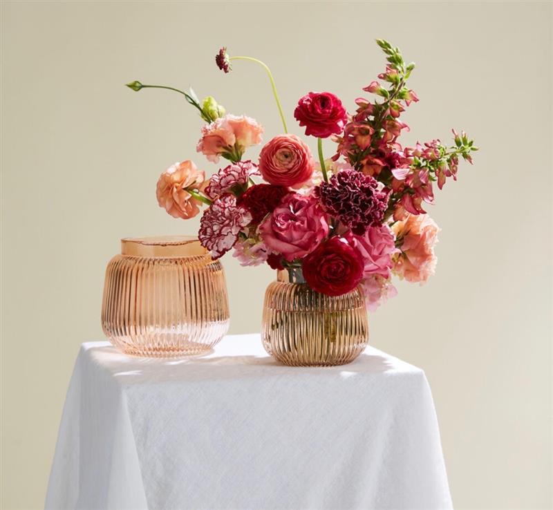 Two elegant vases filled with a vibrant bouquet of red and pink roses, ranunculus, and carnations sit on a white tablecloth in Grand County Colorado.