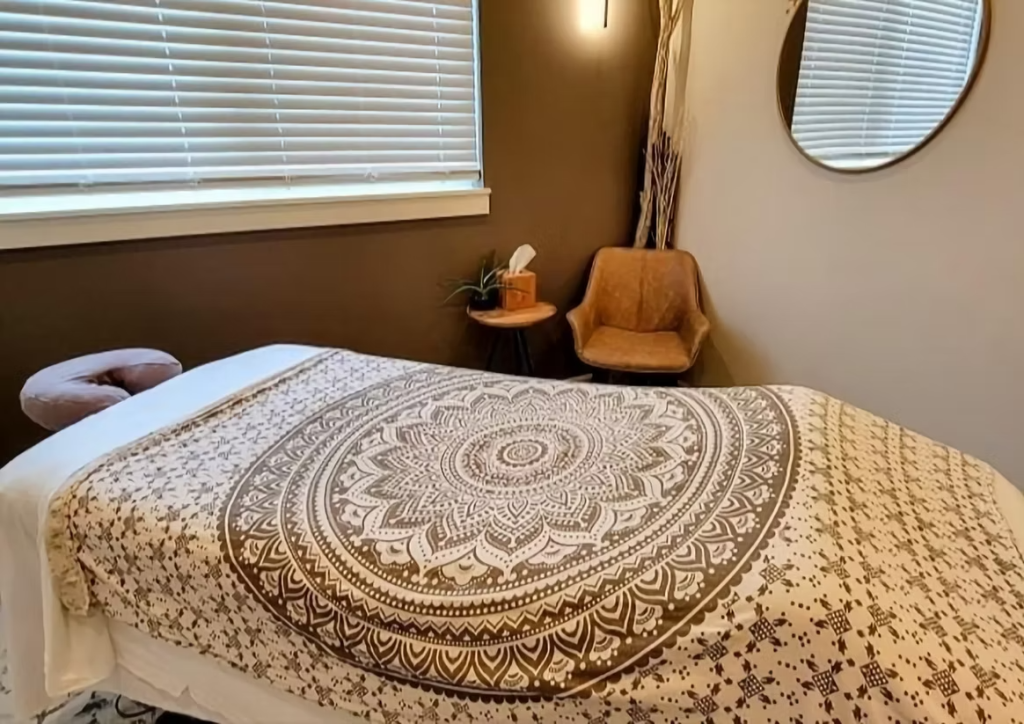 A serene massage therapy room with a table draped in a detailed mandala-patterned blanket, a comfortable chair, and a small plant on a side table in Grand County Colorado.
