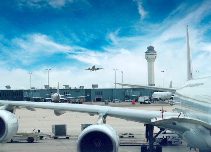A bustling airport tarmac with multiple airplanes, a control tower, and ground support equipment under a partly cloudy sky in Grand County Colorado.