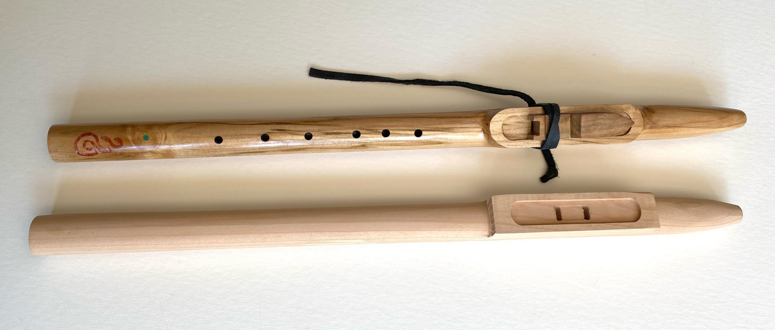 Two wooden flutes, one with intricate carvings and the other plain, lie side by side on a white surface in Grand County Colorado.