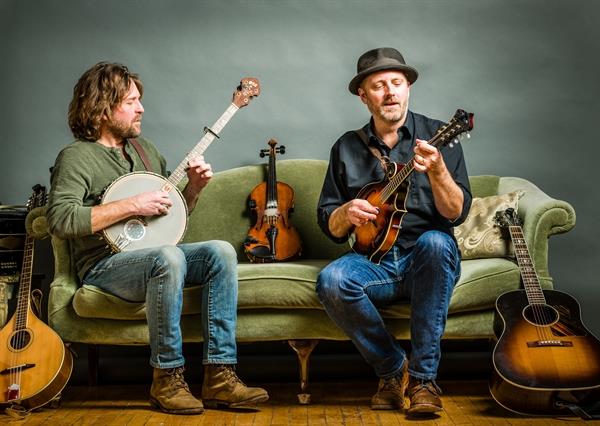 Two musicians play banjo and mandolin on a green couch in Grand County Colorado.