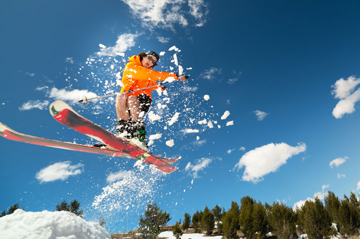 A skier in an orange jacket soars through the air against a backdrop of blue sky and snow-covered trees in Grand County Colorado.