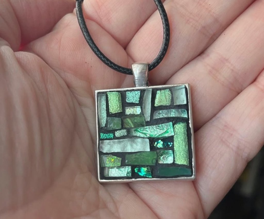 A person holding a square pendant with a mosaic of green and blue glass tiles in Grand County Colorado.