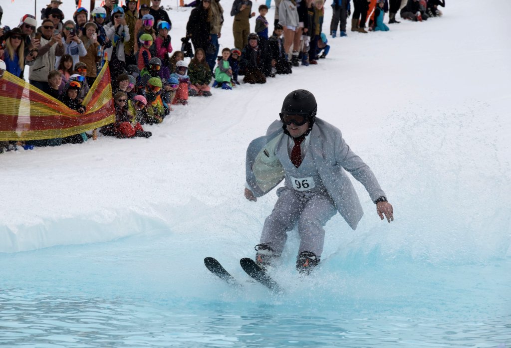 A man in a suit skis through a water-filled ski run, surrounded by spectators in Grand County Colorado.