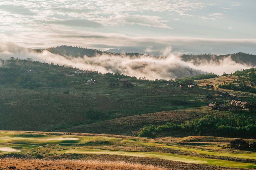 A sprawling view of the rolling hills dotted with trees and buildings, and mist rising over the landscapes in the distance at Granby Ranch.