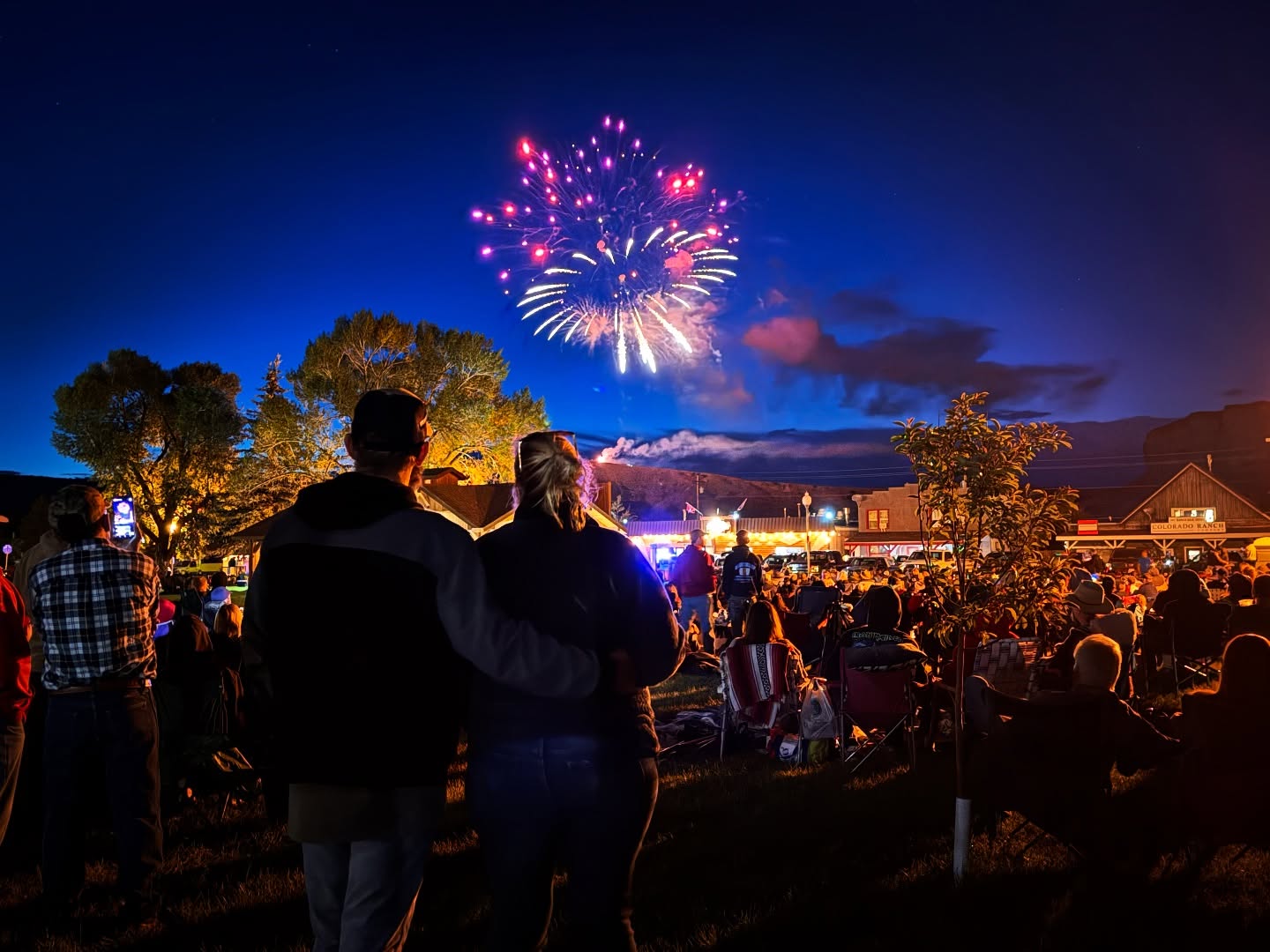 A couple stands hand in hand, gazing up at a dazzling fireworks display lighting up the night sky over a small town in Grand County Colorado.
