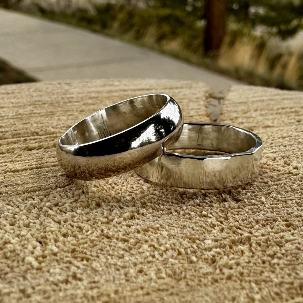 Two silver rings with different finishes are placed on a textured wooden surface in Grand County Colorado.