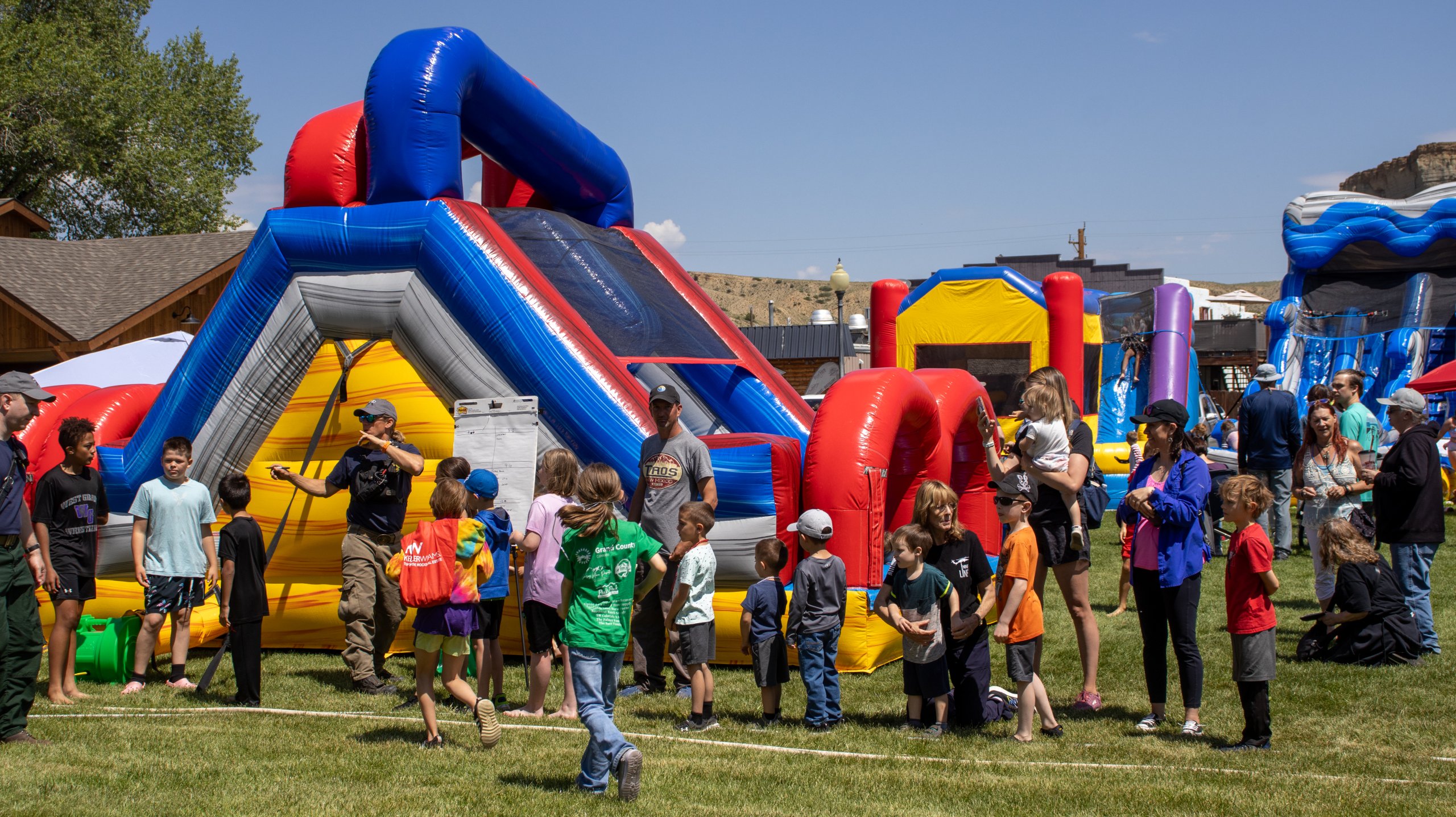 Children and adults enjoy a sunny day at an outdoor inflatable bounce house event in Grand County Colorado.