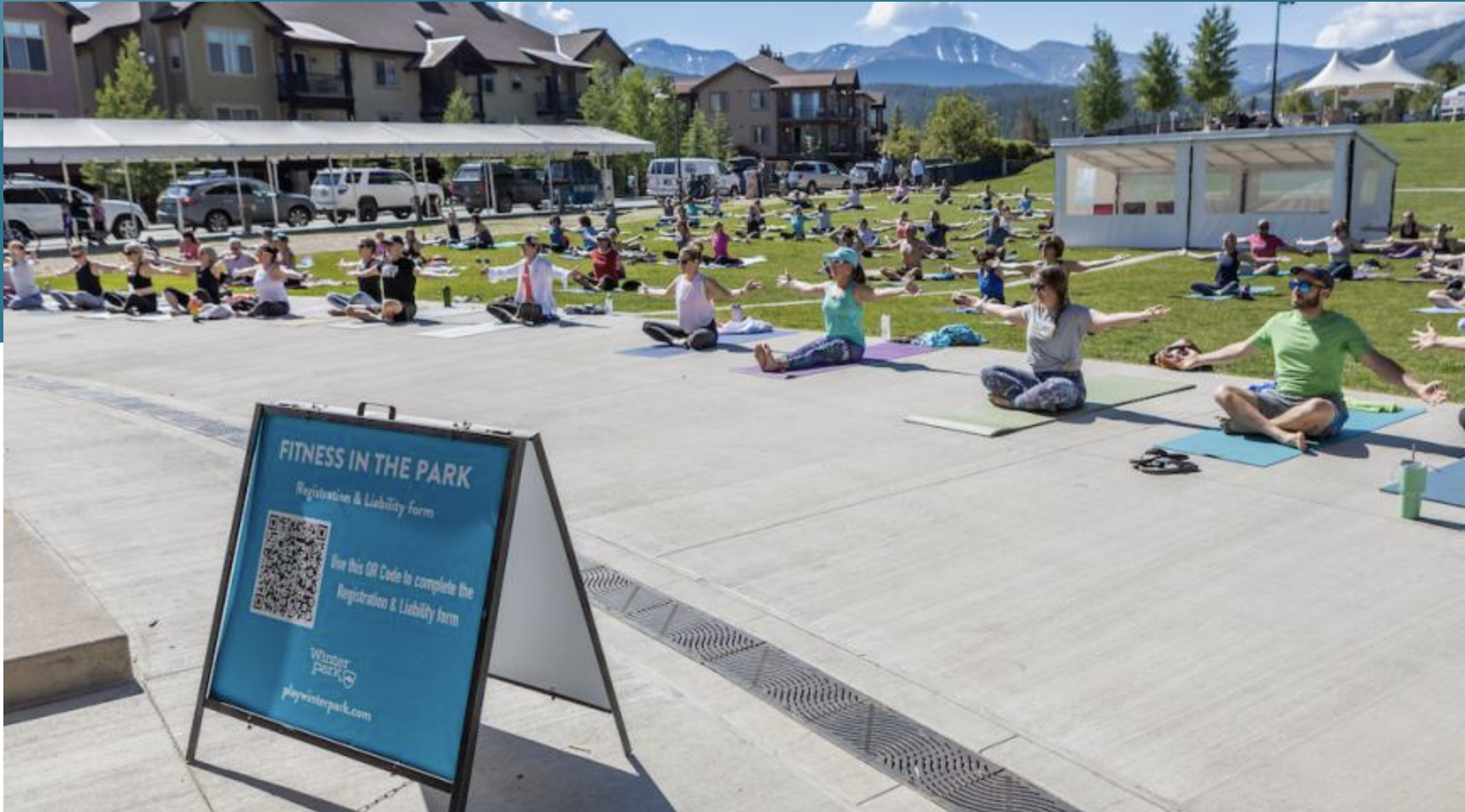 A large group of people practicing yoga outdoors in a park with mountains in the background in Grand County Colorado.
