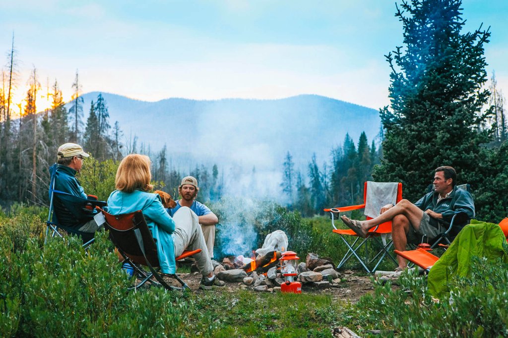 A group of friends enjoys a campfire in a serene mountain meadow at sunset in Grand County Colorado.