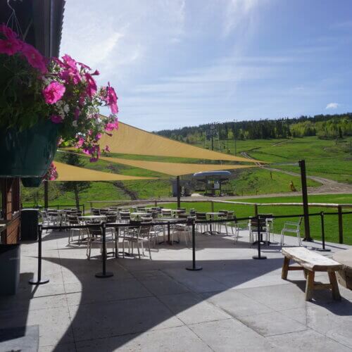 An outdoor patio with tables and chairs under shade sails overlooking a grassy hill in Grand County Colorado.