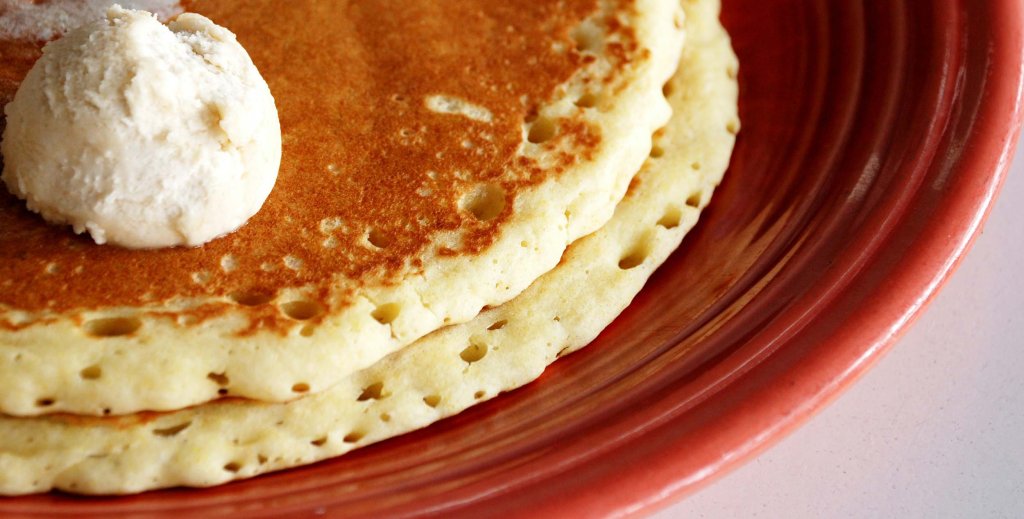 A close-up of a stack of two pancakes topped with butter on a red plate.