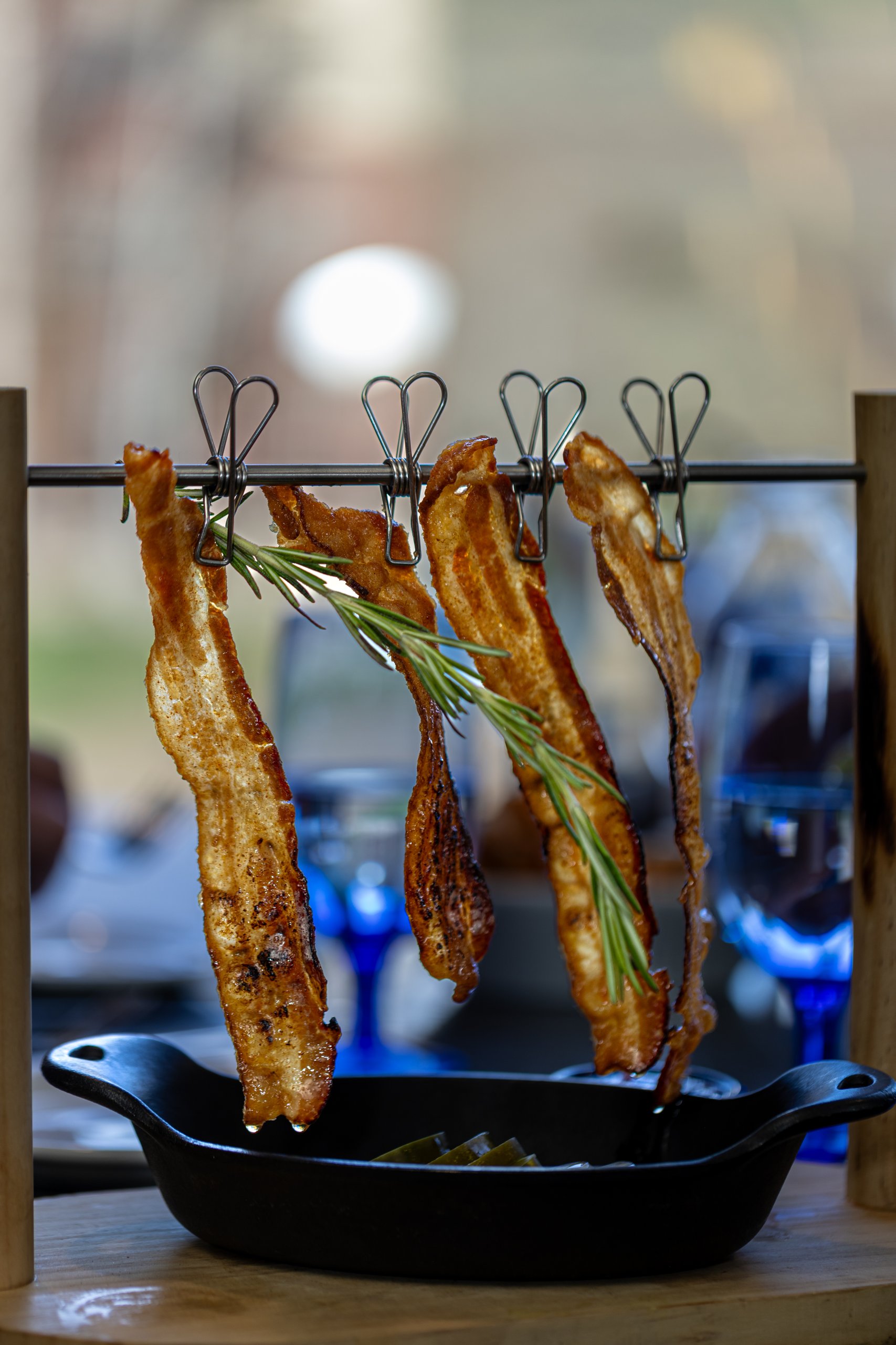 Crispy bacon strips hung on a rack with rosemary sprigs, served in a cast iron skillet in Grand County Colorado.