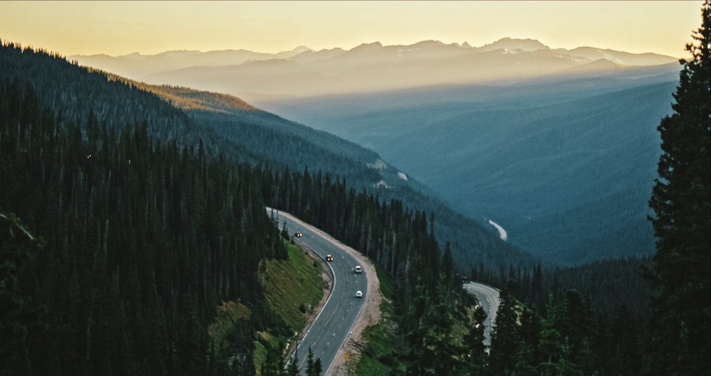 Cars along a road winding through Berthoud Pass, surrounded by thick forests and tree-covered mountains.