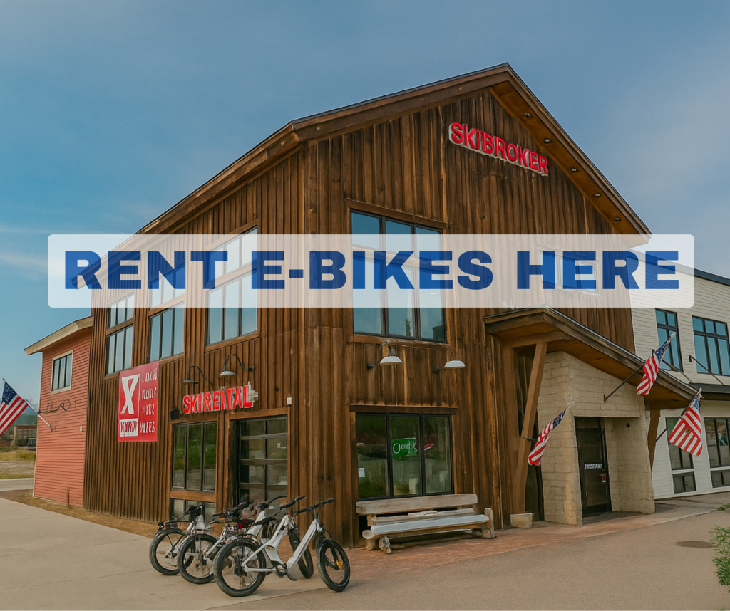 A rustic wooden building with a sign reading 'Skibroker' and 'Rent E-Bikes Here' offers electric bike rentals in a scenic outdoor setting in Grand County Colorado.