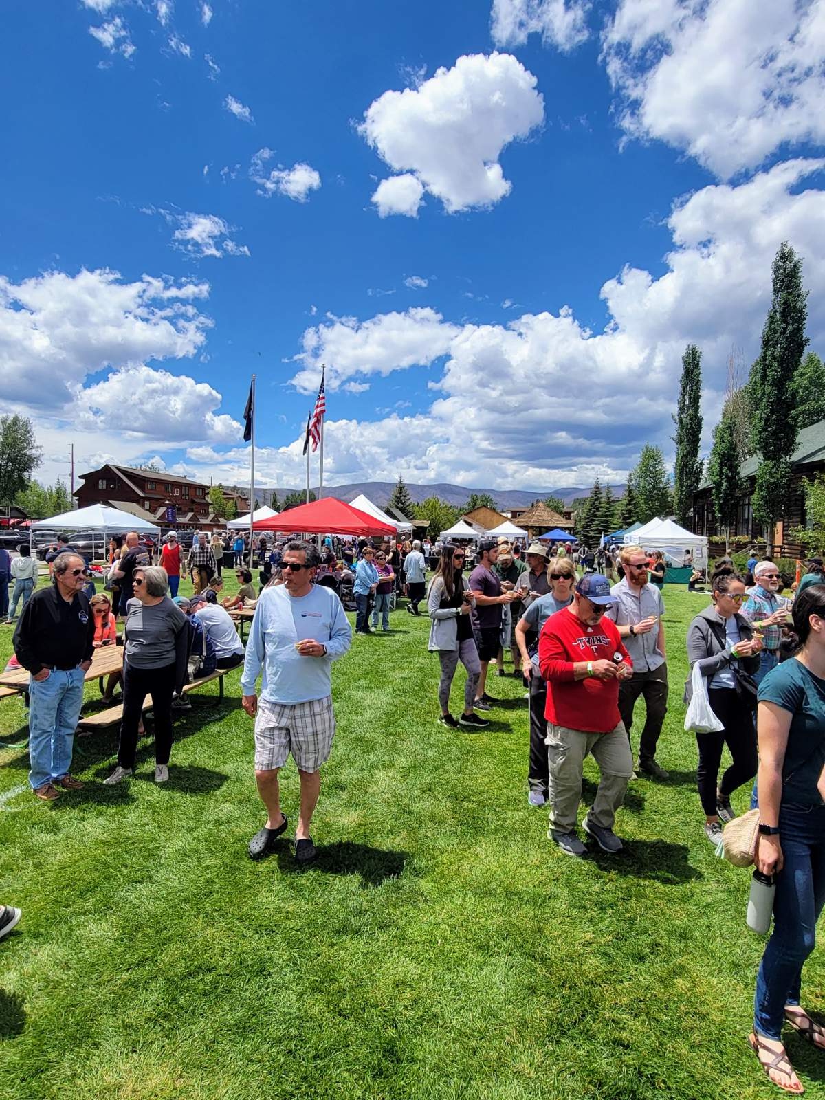 A lively outdoor festival with numerous attendees enjoying food, drinks, and activities under colorful tents on a sunny day in Grand County Colorado.