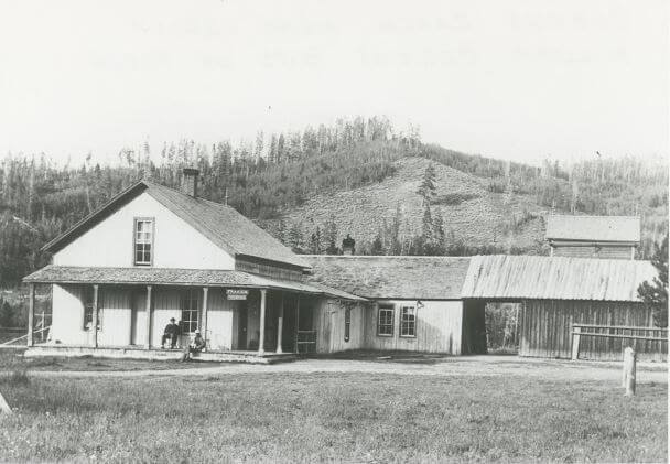 A black and white historic image of Cozens Ranch, showing two people seated on the front porch of a house.