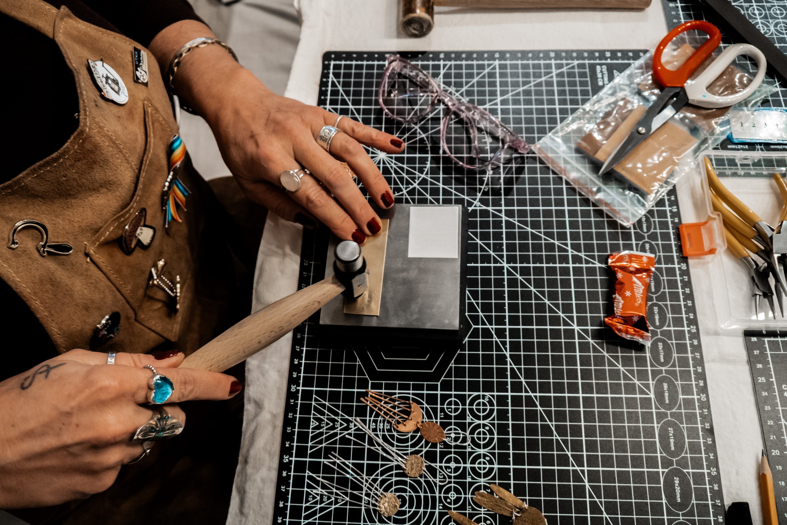 A jeweler meticulously hammers a piece of metal on a workbench, surrounded by tools and materials in Grand County Colorado.