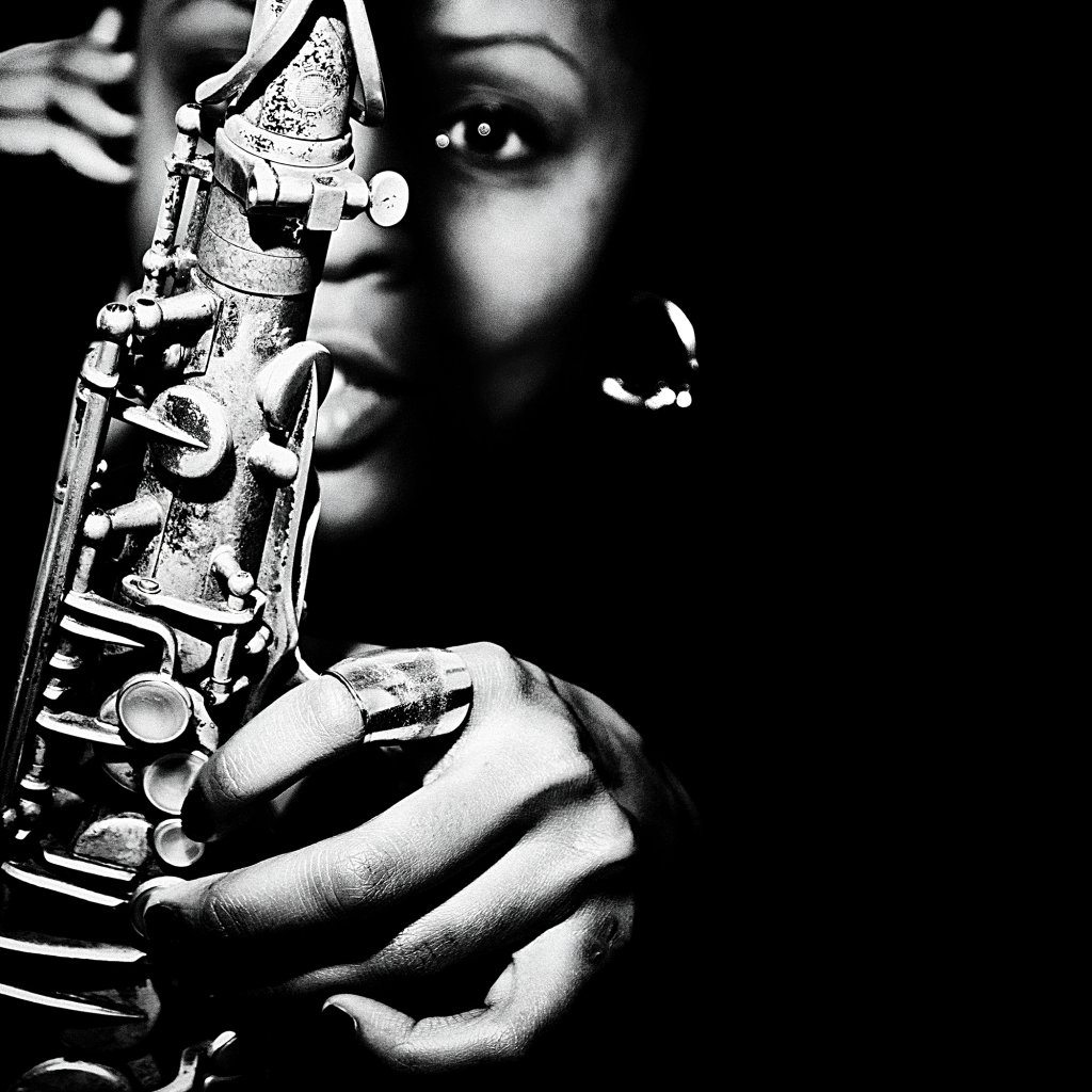 A close-up black and white portrait of a woman playing a saxophone.