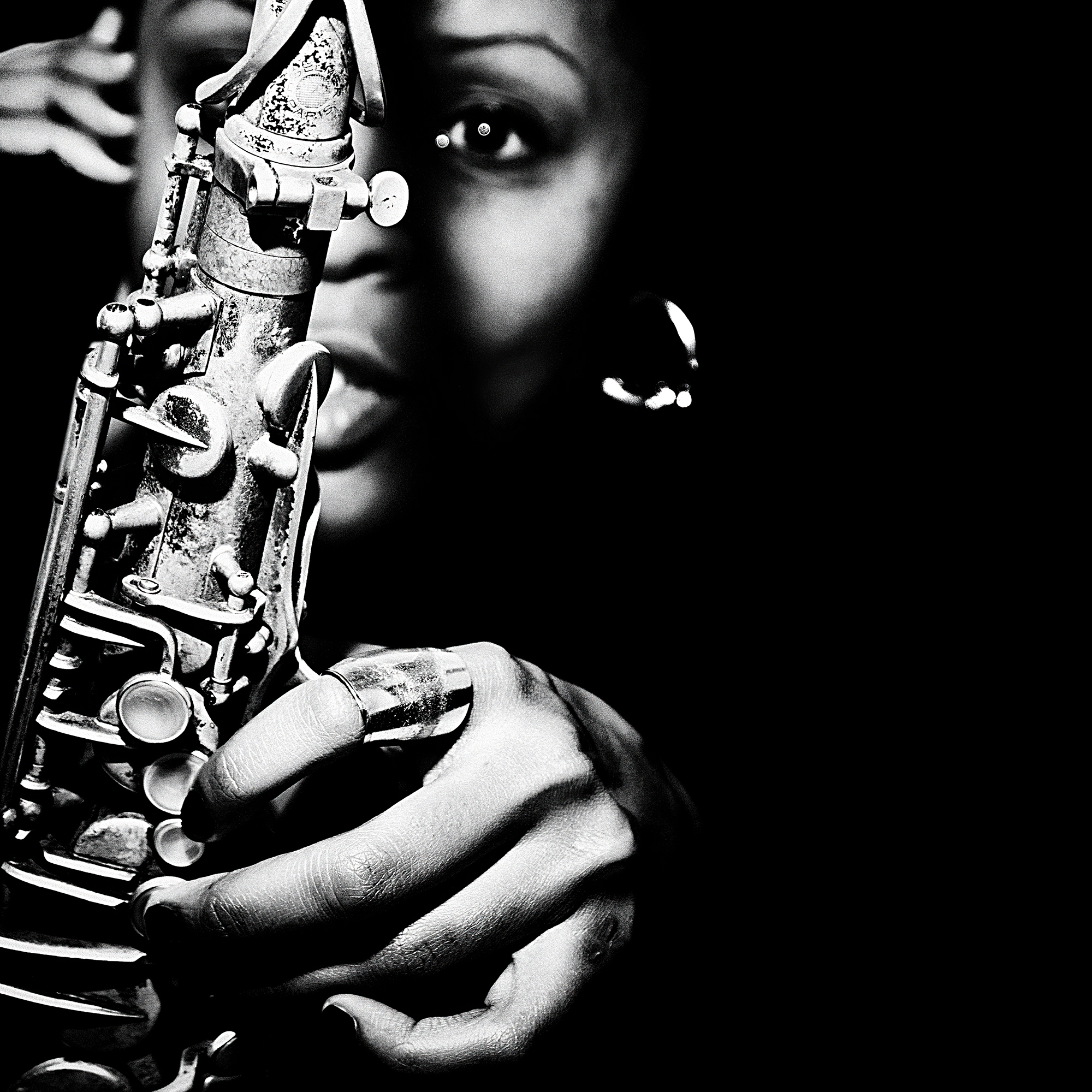 A close-up black and white portrait of a woman playing a saxophone.