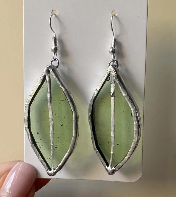 A pair of handmade green stained glass leaf-shaped earrings on a white display card in Grand County Colorado.