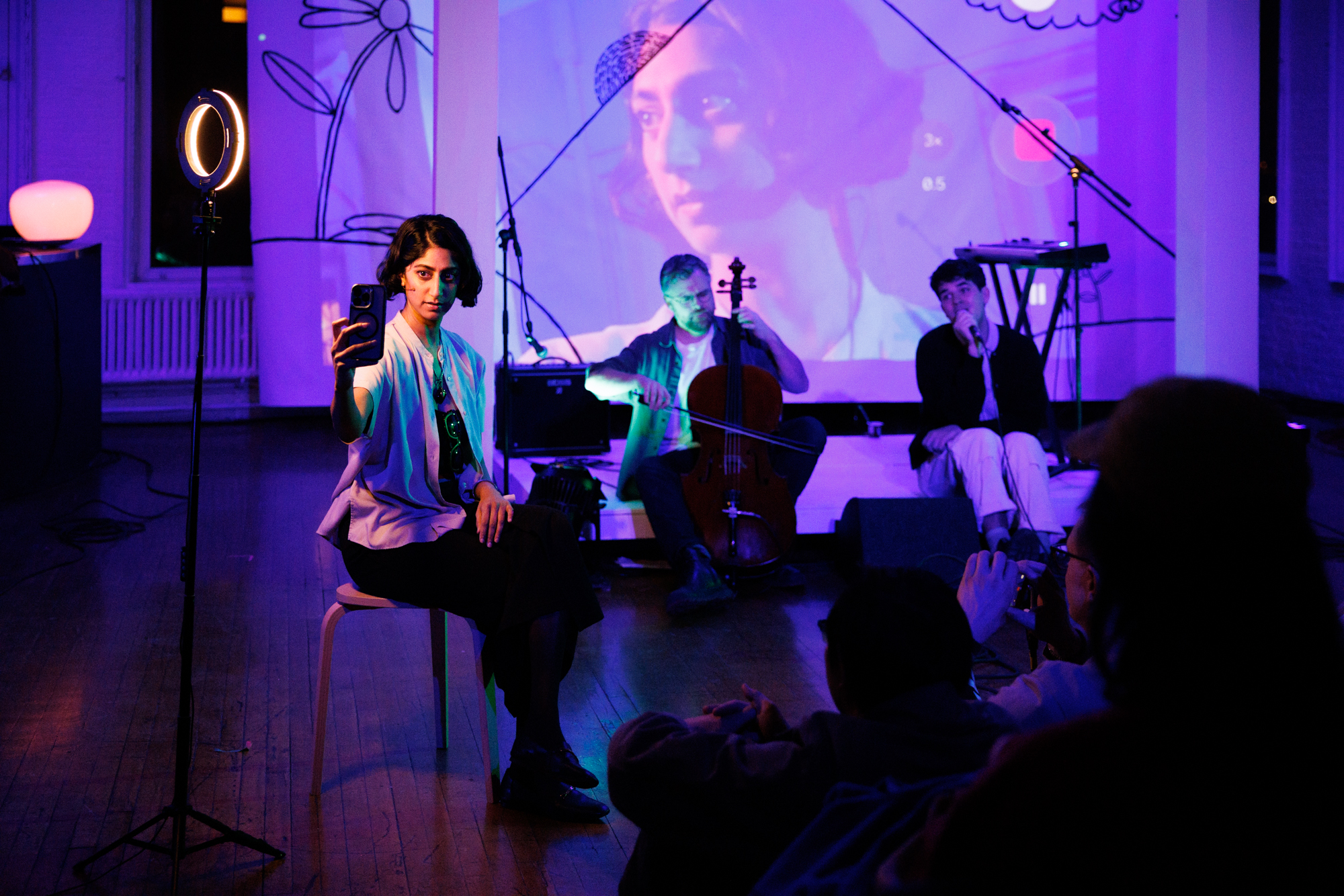 A woman records herself on a phone while musicians perform on a purple-lit stage in Grand County Colorado.