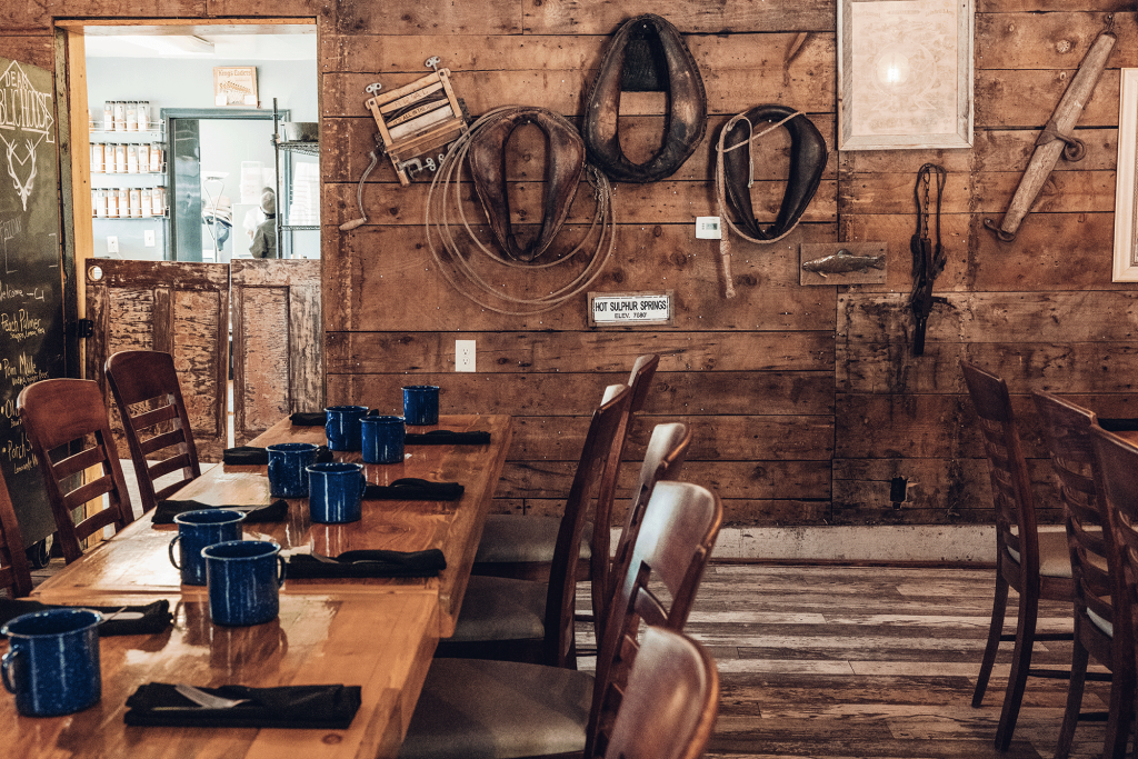 Interior of Dean’s Public House featuring rustic wood-paneled walls, wooden dining tables, blue enamel mugs and historic ranching equipment.
