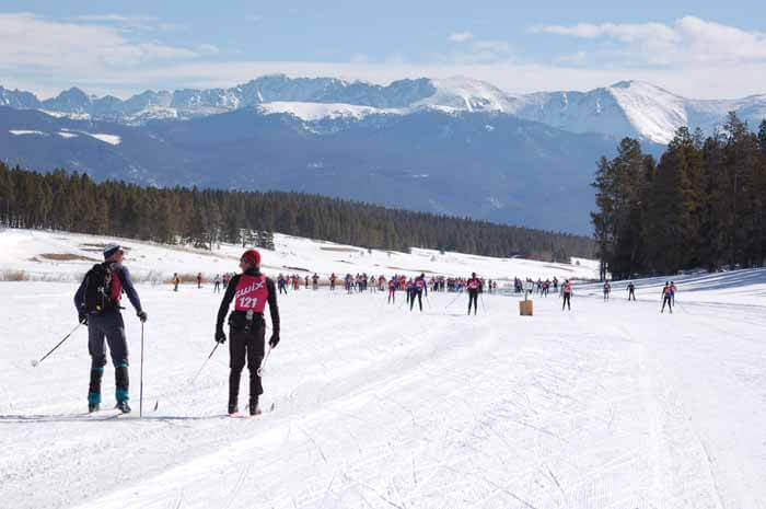 Cross-country skiers gather on a snowy field with mountains in the background in Grand County Colorado.