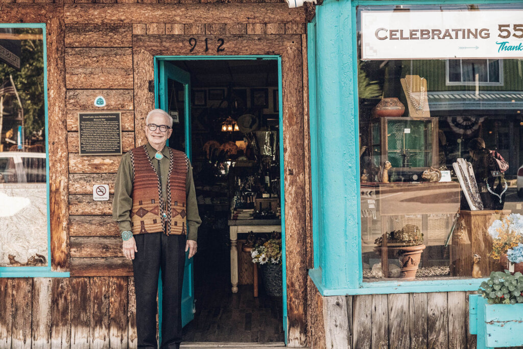 An elderly man in a patterned vest stands in the doorway of a rustic shop in Grand County Colorado.