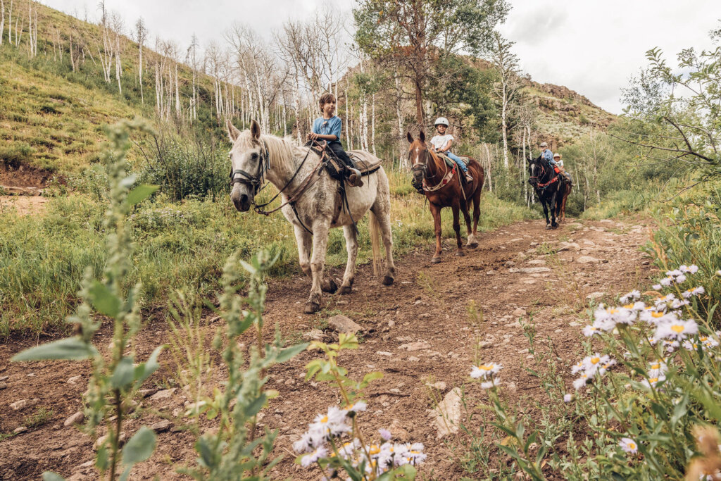 Three children riding horses along a dirt trail in a mountainous forest in Grand County Colorado.