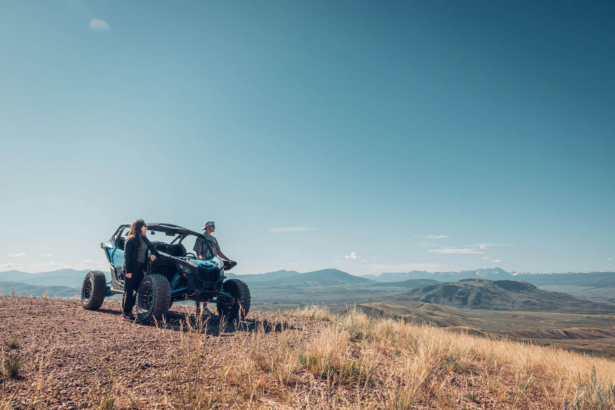 A couple stands next to an off-road vehicle overlooking a vast mountain landscape in Grand County Colorado.