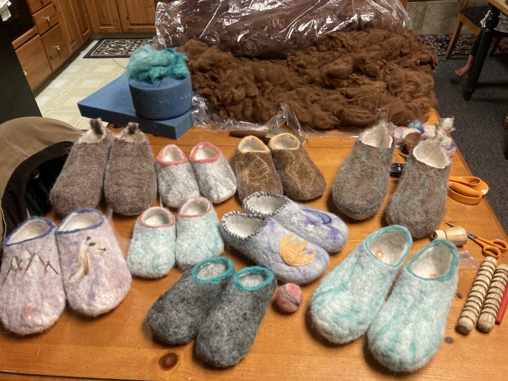 Many pairs of handmade felted wool slippers arranged on a wooden table in Grand County Colorado.