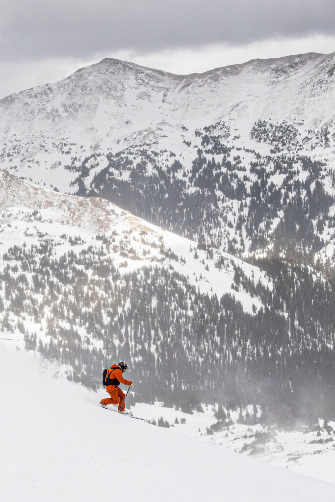 A skier in an orange suit skiing down a snowy mountain slope in Grand County Colorado.